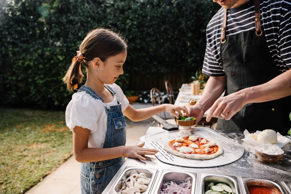 Kind belegt Pizza an der Everdure Pizza Station im Garten